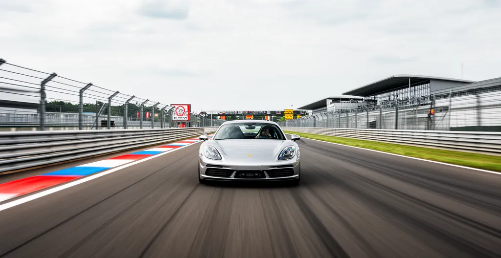 Voiture de sport type Porsche roulant sur circuit automobile avec vibreurs visibles